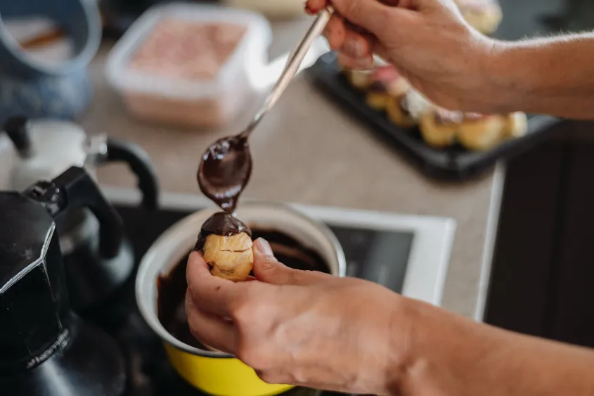 A catering person pouring chocolate onto a profiterole